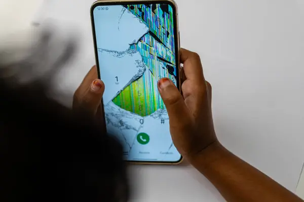 Ciddi bir şekilde çatlamış ve bozulmuş ekranlı akıllı telefonu tutan eller bir arama yapmaya çalışıyor. Teknik aksilik, tamir gerekli..