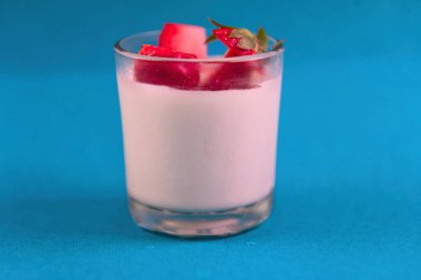 Bir bardak çilek aromalı süt. Bardağın yarısı dolu. Sütün üstünde çilek var.