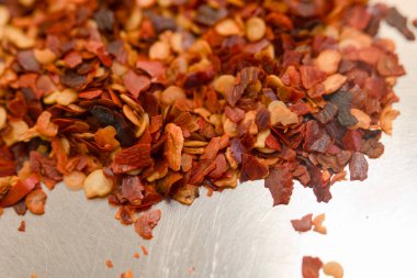 Kurumuş kırmızı biber tanelerinin canlı bir karışımı pürüzsüz bir metal yüzeye saçılmış, çeşitli renk ve dokular sergiliyor..