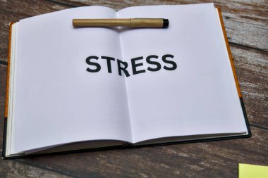 Stres kelimesinin kullanıldığı ahşap bir yüzey üzerine açık bir defter okuyucuları stres azaltma yöntemlerini keşfetmeye teşvik ediyor..