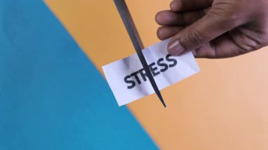 Renkli bir arkaplandaki stresi, rahatlık ve refahı simgeleyen bir kartı kesmek için makas kullanan bir el..