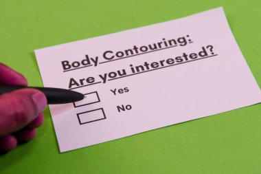 Bir kişi, canlı yeşil bir yüzey üzerinde siyah bir kalem kullanarak vücut hatlarıyla ilgili bir anket kartına ilgi gösteriyor..