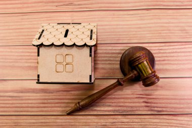 Ahşap bir ev modeli, bir tokmağın yanında oturuyor. Odaklanmış bir tartışma sırasında gayrimenkuldeki yasal meseleleri temsil ediyor..