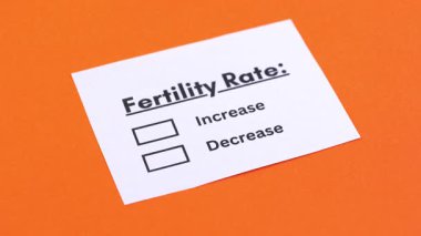 Birisi parlak turuncu arka planda doğurganlık oranlarını gösteren bir kutucuğu kalemle işaretliyor..