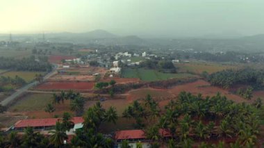 Sakin bir insansız hava aracı manzarası, bereketli tarlaları, dolambaçlı yolları, dağınık evleri, palmiye ağaçlarını ve uzak tepeleri olan pitoresk bir kırsal alanı gösteriyor..
