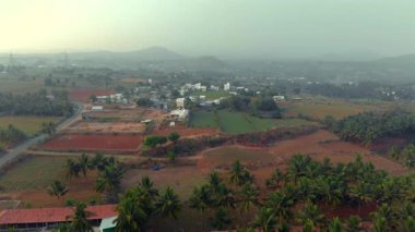 Sakin bir insansız hava aracı manzarası, bereketli tarlaları, dolambaçlı yolları, dağınık evleri, palmiye ağaçlarını ve uzak tepeleri olan pitoresk bir kırsal alanı gösteriyor..
