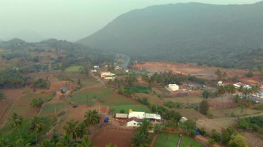 Hava manzaralı sakin bir kırsal alan, tarlalar, evler ve şafak vakti sisli dağların arasında dolambaçlı bir yol yakalıyor..