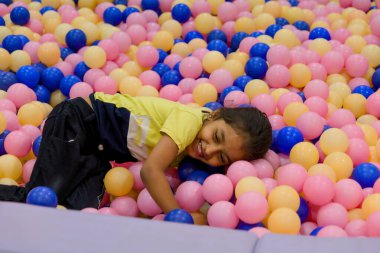 Genç bir kız pembe ve mavi toplarla dolu canlı bir top havuzunda yuvarlanıp gülmekten zevk alır..