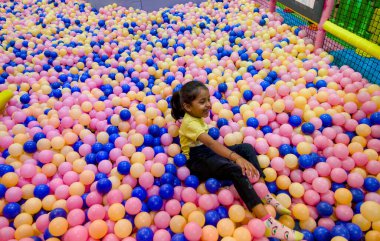 Genç kız, renkli plastik toplarla dolu canlı bir top havuzunda otururken eğleniyor..