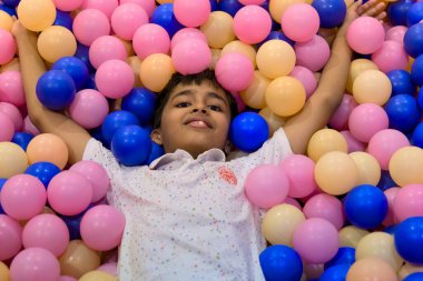 Genç çocuk oyun sahasında pembe, mavi ve sarı toplarla dolu bir top havuzunda uzanmaktan zevk alıyor..