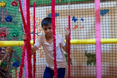 Genç bir çocuk, tırmanma engelleri ve parlak dekorasyonlarla dolu eğlenceli ve canlı bir oyun bahçesinde yol alıyor..