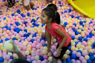 Çocuklar pembe ve mavi taşaklarla dolu canlı bir top havuzunda gülüyor ve oynuyorlar..