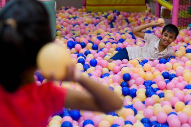 İki çocuk canlı bir top havuzunda, birbirlerine top fırlatma oyunuyla eğleniyorlar..