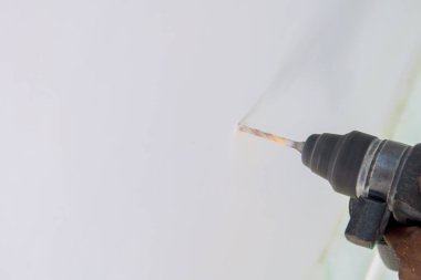 Ev tadilatı sırasında beyaz bir duvarda delik açan matkabın yakın çekimi..