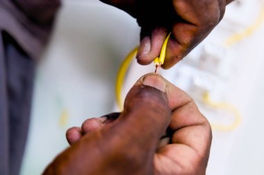 Sarı bir elektrik kablosundan yalıtım malzemesi soyan ellerin yakın görüntüsü..