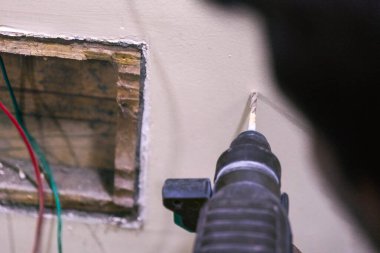 İşçi, duvarda elektrik tesisatı için bir delik açmak ve bir projede ev yenileme çalışması yapmak için matkap kullanıyor..