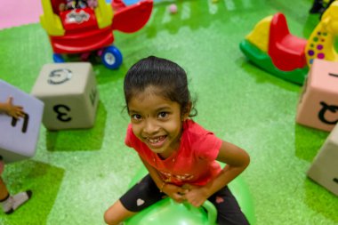 Genç kız oyuncaklarla dolu renkli bir oyun alanında yeşil şişirilebilir bir alanda zıplamaktan hoşlanıyor..