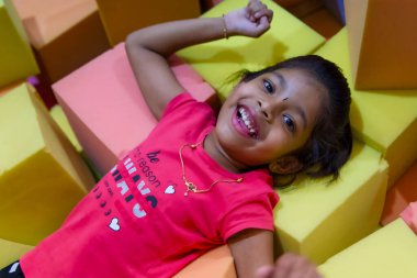 Küçük kız yumuşak köpük bloklarda yatarken neşeli bir şekilde gülümsemeyi sever..