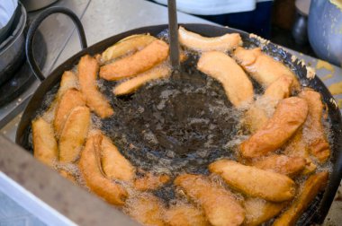 Kızarmış altın muzlar kızgın yağda cızırdıyor, canlı bir mutfak ortamında yemek pişirme sürecini sergiliyor..