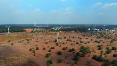 Rüzgâr türbinleri, kırsal bölgelerde sürdürülebilir enerjiyi teşvik eden uçsuz bucaksız bir arazinin üzerindeki açık mavi gökyüzünde dimdik dururlar..