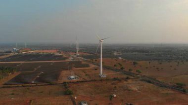 Gündüz sisli bir gökyüzünün altında kırsal bir alanda rüzgar türbinleri ve güneş panelleri olan yenilenebilir enerji sistemi.