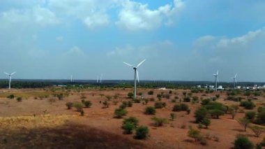 Rüzgâr türbinleri uçsuz bucaksız kırsal bir alanda, açık mavi gökyüzünün altında dağınık bulutlarla birlikte enerjilerini dizginleyerek dimdik ayakta duruyorlar..