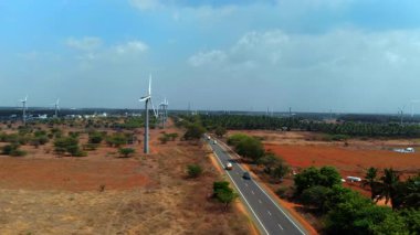 Rüzgâr türbinleri, kırsal alanda dolambaçlı bir yolun kenarında, parlak bir arazide temiz enerji sergilerler..