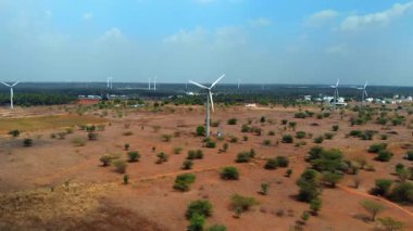 Rüzgâr türbinleri kurak bir arazide dimdik ayakta duruyor, berrak bir gökyüzünün altındaki seyrek bitki örtüsünün arasında yenilenebilir enerjiden faydalanıyor..