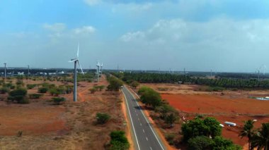 Parlak mavi gökyüzünün altında bir otoyol boyunca rüzgar türbinlerinin yer aldığı geniş kırsal alan..