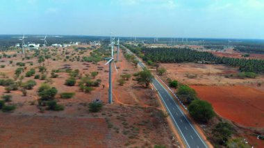 Kırsal bir yolda rüzgar türbinleri yükseliyor, canlı bir tarım arazisinde sürdürülebilir enerjiyi vurguluyorlar..
