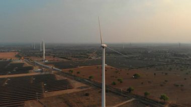 Güneş panelleri üzerinde dönen rüzgar türbinleri günbatımında geniş bir yenilenebilir enerji alanında sürdürülebilir teknoloji sergiliyor..