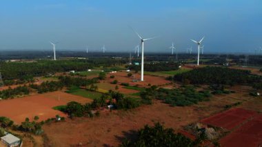 Rüzgâr türbinleri canlı bir kırsalda, berrak bir gökyüzüne karşı yükselirler ve dingin, yenilenebilir enerji üretimi sergilerler..