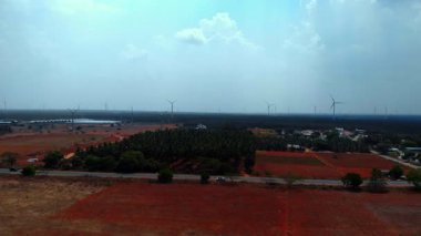 Gündüz vakti kırsal alanda rüzgâr türbinleri, tarım arazileri ve açık gökyüzünü gösteren geniş bir manzara..