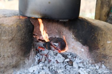 Su, açık ateşin üzerinde bir tencerede kaynıyor. Geleneksel yemek pişirme yöntemleri ve doğal ısı kaynakları sergileniyor..