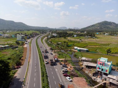 Hava perspektifi, yemyeşil tarlalar ve açık bir gökyüzünün altındaki uzak dağlarla çevrili bir otoyol gösteriyor..