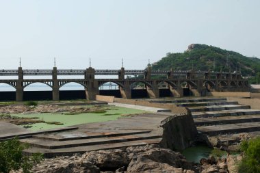 Büyük bir köprü, açık mavi gökyüzünün altında yeşilimsi bir alanı olan kavrulmuş bir nehir yatağını kaplar..