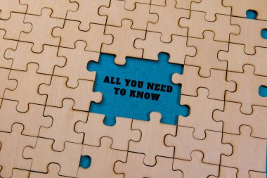 Bir çalışma alanındaki kısmen tamamlanmış ahşap yapboz mavi bir arkaplanda 'Tüm bilmeniz gerekenler' cümlesini içerir.