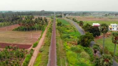 Demiryolları açık gökyüzünün altındaki yemyeşil alanlar boyunca uzanıyor, kırsal yaşam ve tarımı gözler önüne seriyor..