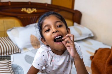 Genç bir kız, yumuşak yatak odası ve peluş oyuncaklarla çevrili, rahat bir yatak odasında kurabiye yerken gülümsüyor..