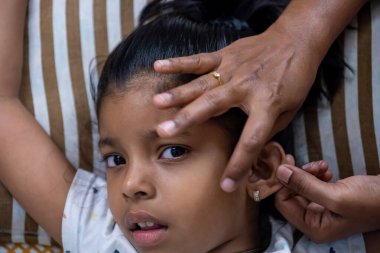 Genç bir kız, evde rahat bir ortamda kulağını ustalıkla delen bir yetişkin gibi görünürken kararsız görünüyor..