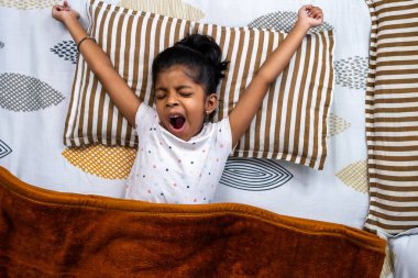 Genç bir çocuk yatakta uyanırken esniyor, parlak bir sabah başlangıcı ve rahat bir atmosfer gösteriyor..