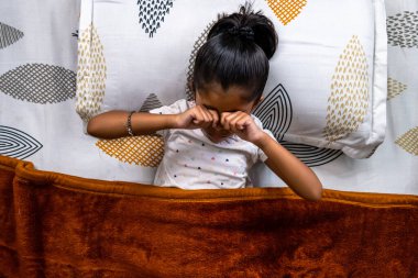 Küçük çocuk, sabah saatlerinde yumuşak battaniyeler ve renkli yastıklarla sıcak, rahat bir yatakta dinlenirken uyanır..