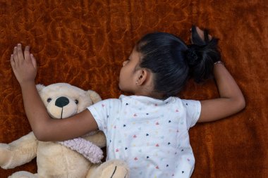 Genç bir çocuk sıcak bir battaniyenin üzerinde dinleniyor, oyuncak ayıya sarılıyor, huzurlu ve rahatlatıcı bir atmosfer yaratıyor..