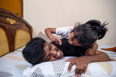 Bir baba ve küçük kızı bir yatakta rahatça oynarken keyifli bir anı paylaşıyorlar..