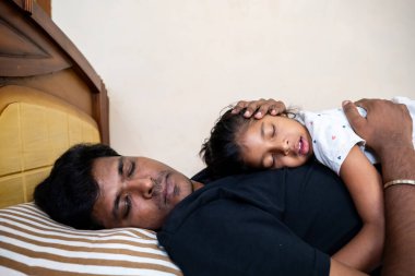 Bir baba ve kızı, bir yatakta uyurken, sevgi ve şefkat göstererek huzurlu bir anı paylaşırlar..