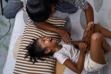 Bir kız, gün boyunca sıcak bir evde bakıcısıyla yatakta oynarken neşeyle güler..