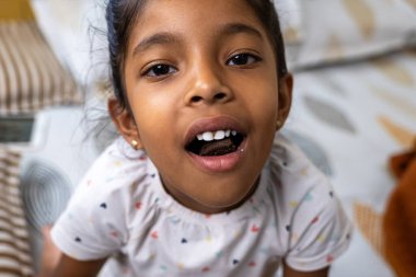 Genç kız, yumuşak yastıklar ve battaniyelerle süslenmiş rahat bir yatakta otururken dişlerini neşeyle sergiliyor..