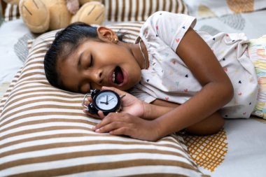 Genç kız içi doldurulmuş oyuncaklarla dolu bir yastıkta elinde saatle huzur içinde uyuyor..