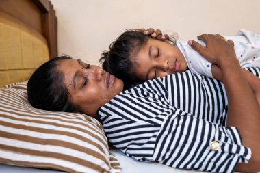 Bir anne ve kızı, sakin bir ortamda rahat bir yatakta yatarken hassas bir anı paylaşıyorlar..