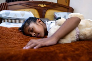 Genç bir kız rahat bir yatakta uyuyor, sıcak ve davetkar bir yatak odasında oyuncak ayıya sarılıyor..